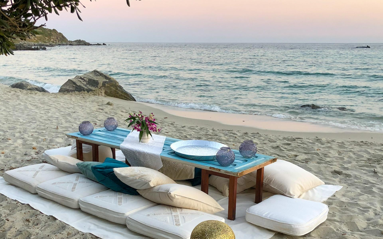 Sunset beach dinner setup with cushions and lanterns